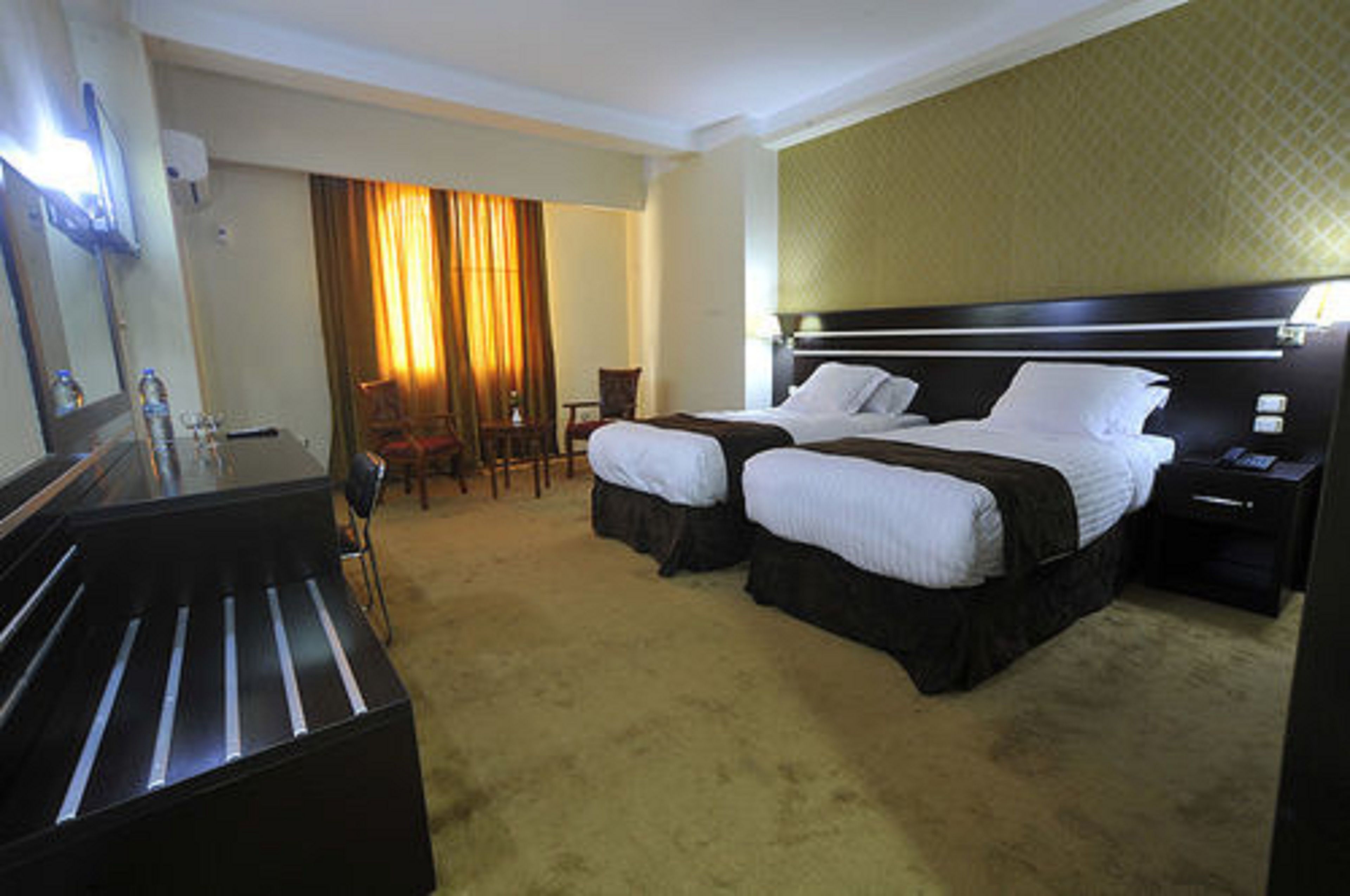 Habitación de hotel con dos camas, un escritorio, una silla y un espejo grande.