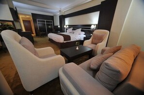 A modern hotel room with a large bed, two armchairs, a sofa, and a small coffee table.