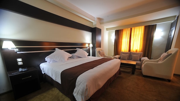 Una habitación de hotel con una cama grande, dos sillones, una mesita y una mesita de noche con lámpara.