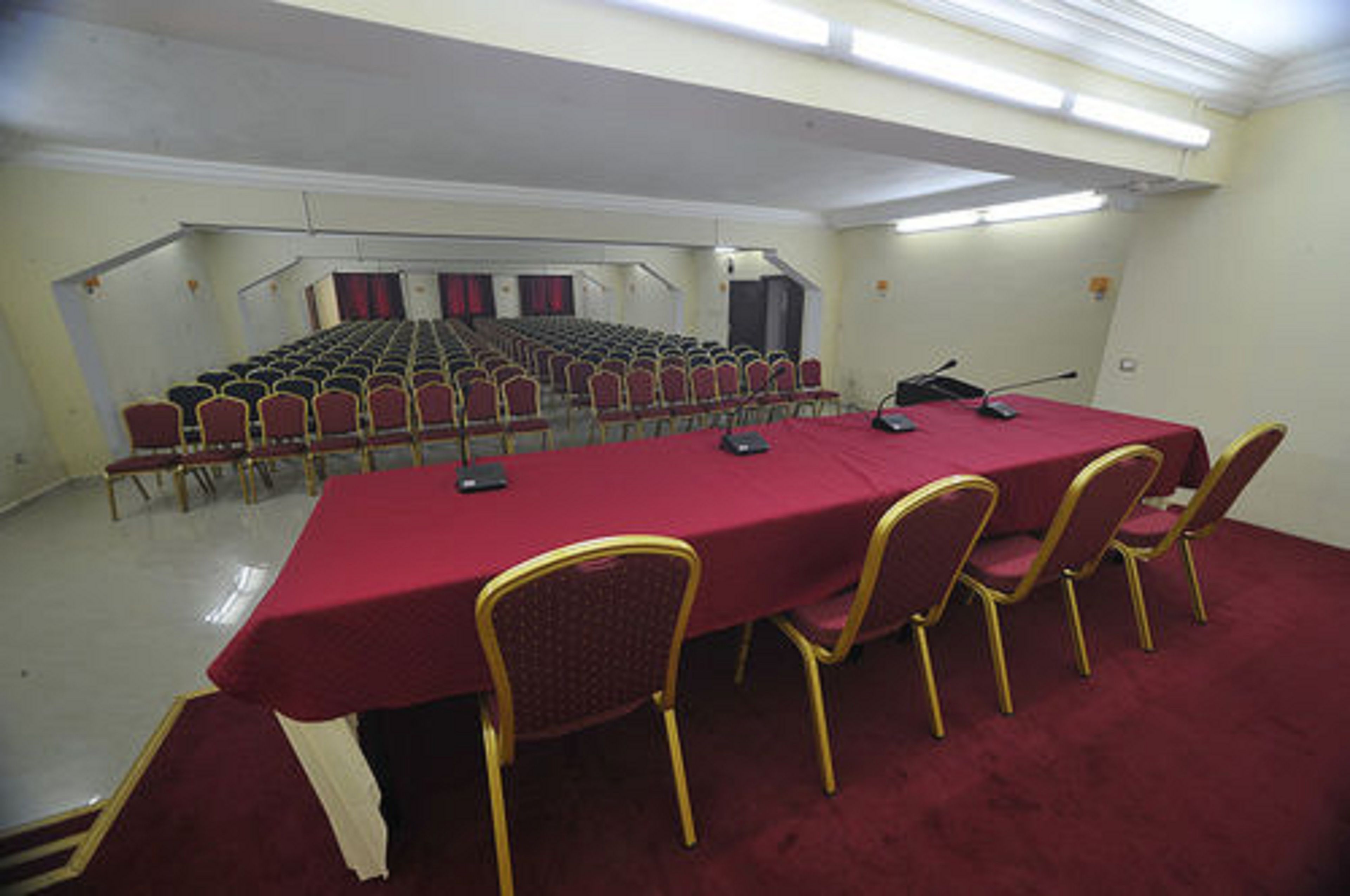 Un salón de conferencias con una larga mesa, filas de sillas y una zona de escenario.