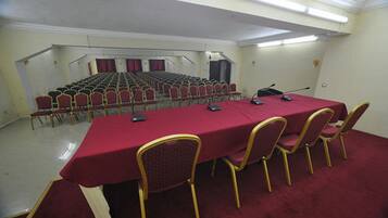 Un salón de conferencias con una larga mesa, filas de sillas y una zona de escenario.