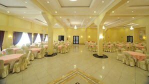 Un salón de banquetes con mesas y sillas redondas, una araña y suelo de baldosas.