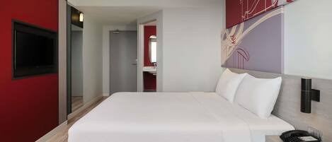 A modern hotel room with a large bed, a flat-screen TV, a bedside table, and a red accent wall.