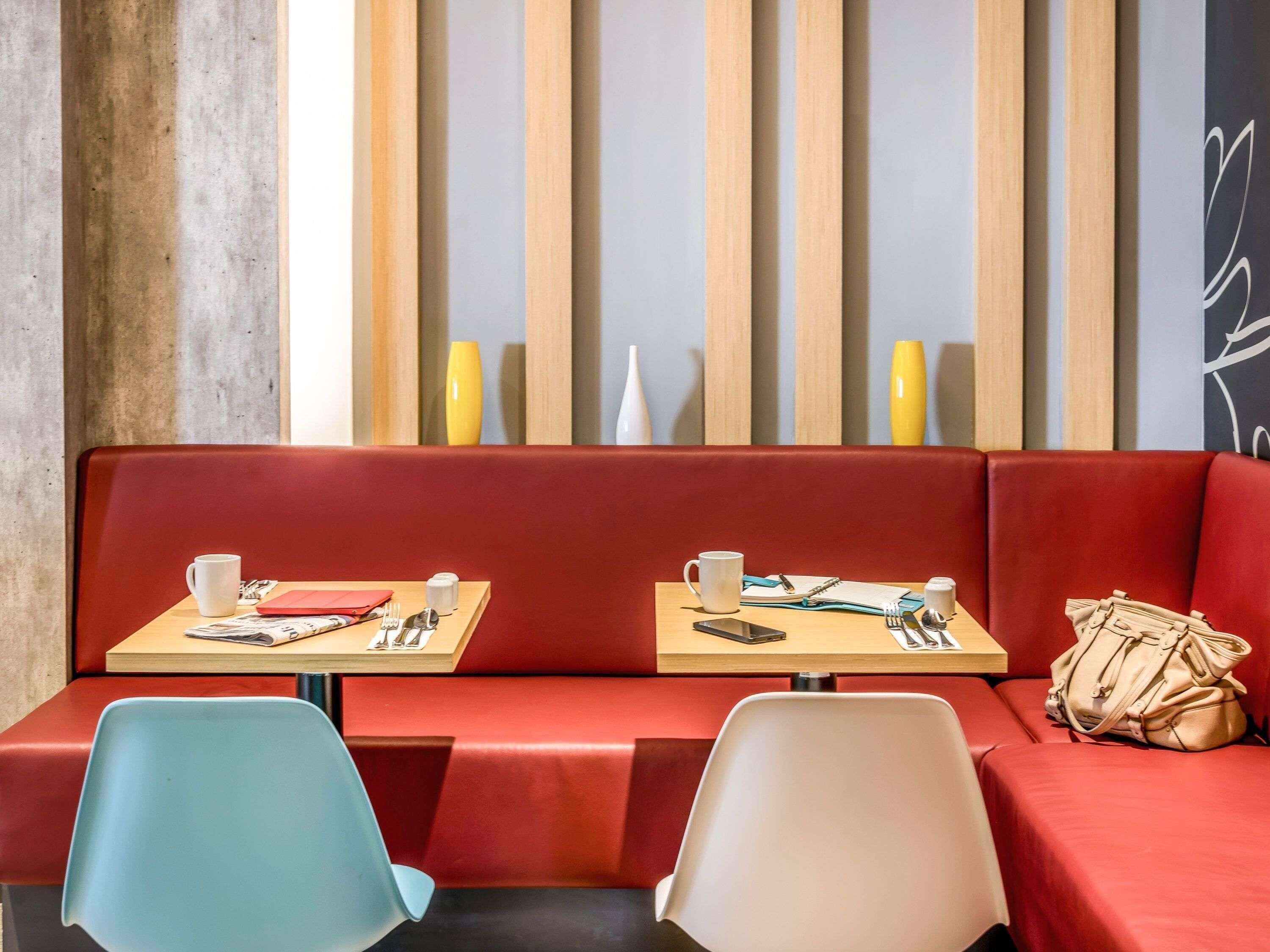 A modern seating area with a red cushioned bench, two tables with chairs, and a decorative wall with vertical wooden slats and vases.