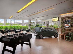 A modern indoor space with a foosball table, a vintage car, and a view of greenery outside. - ibis Bangkok IMPACT (Pak Kret)