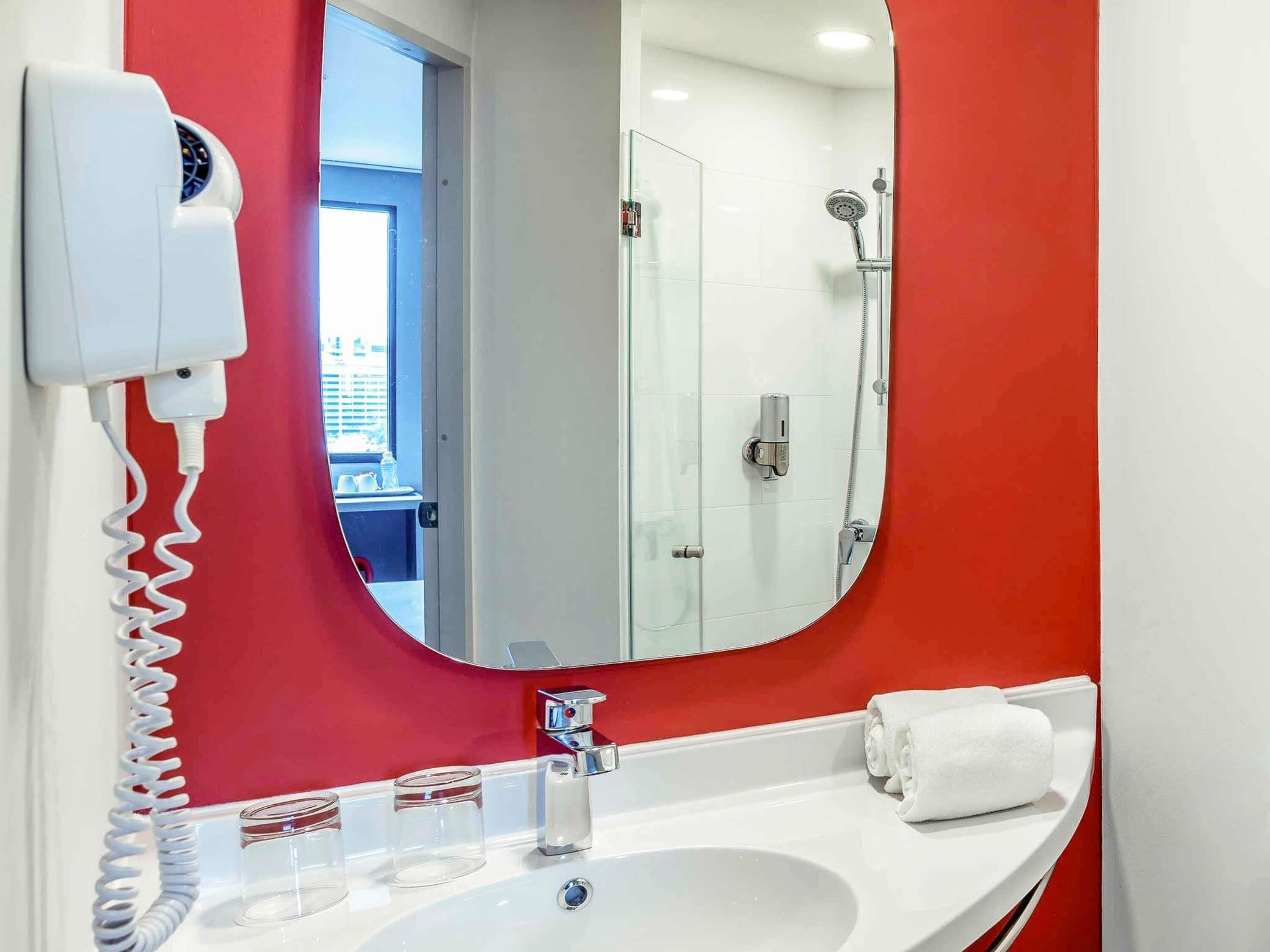 Un baño con lavamanos blanco, espejo, secador de pelo y ducha.