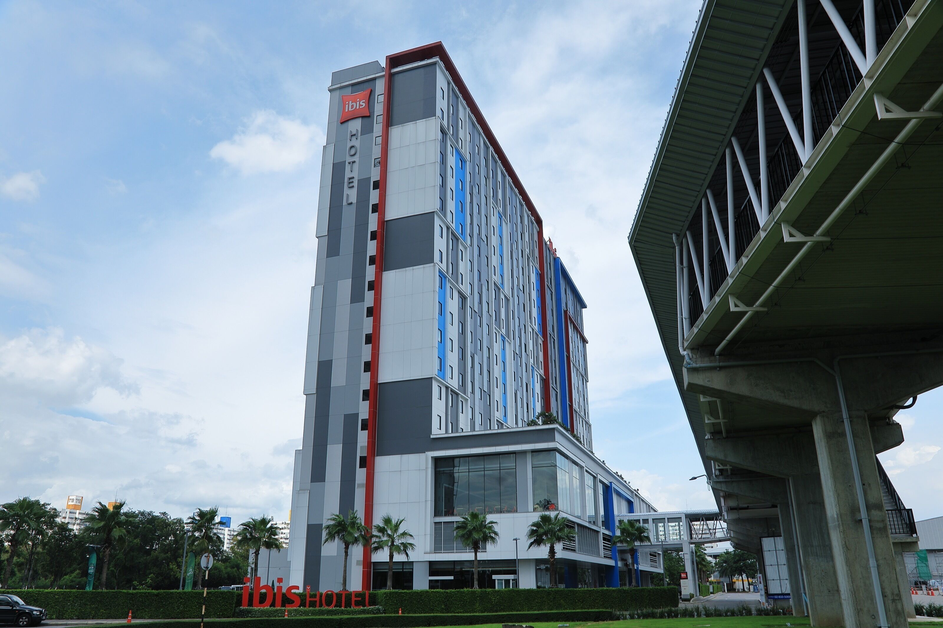A modern hotel with a prominent 'ibis' sign, multiple floors, and a large glass facade.