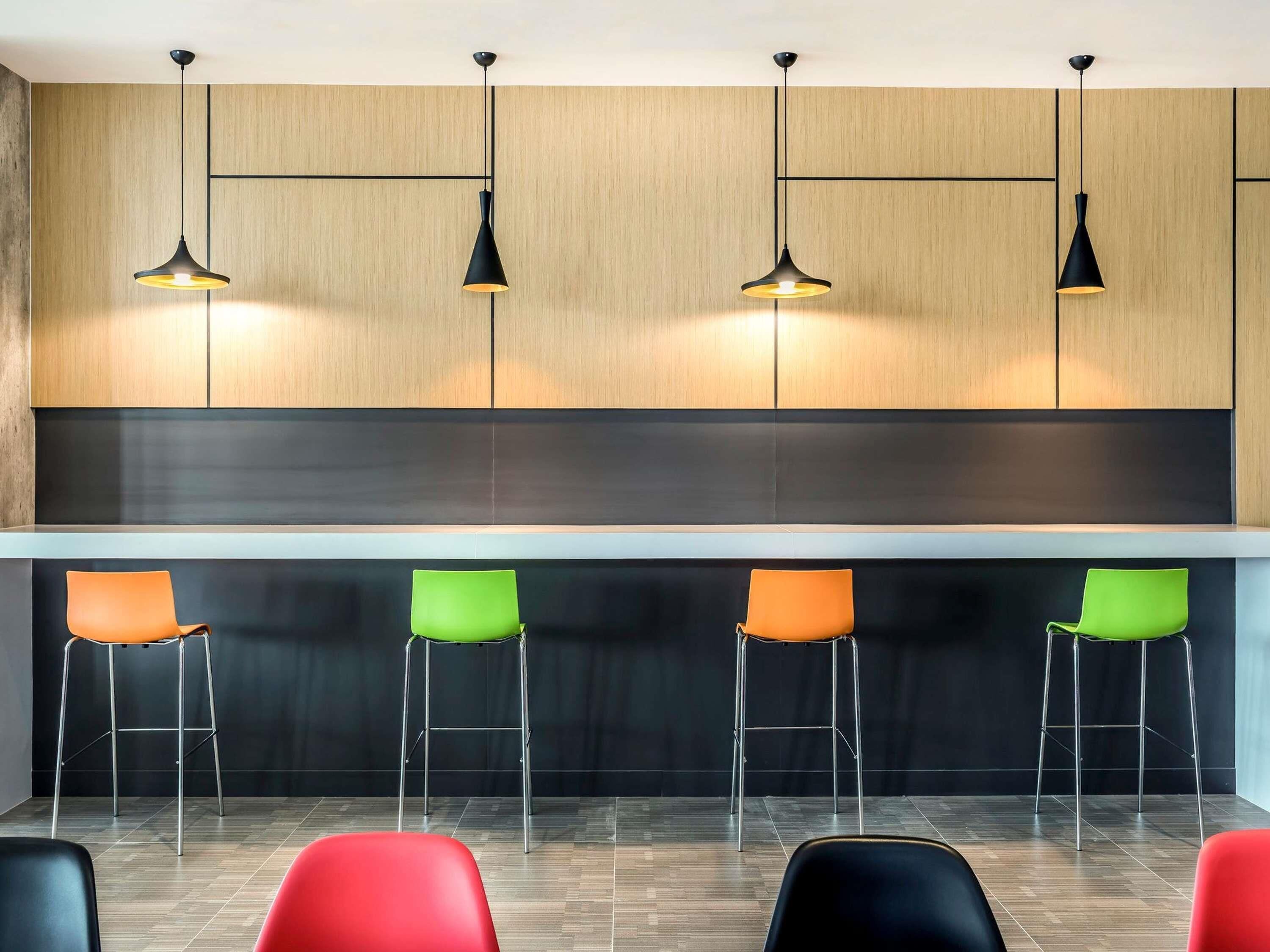 A modern kitchen with four pendant lights, a black countertop, and four bar stools with green and orange seats.