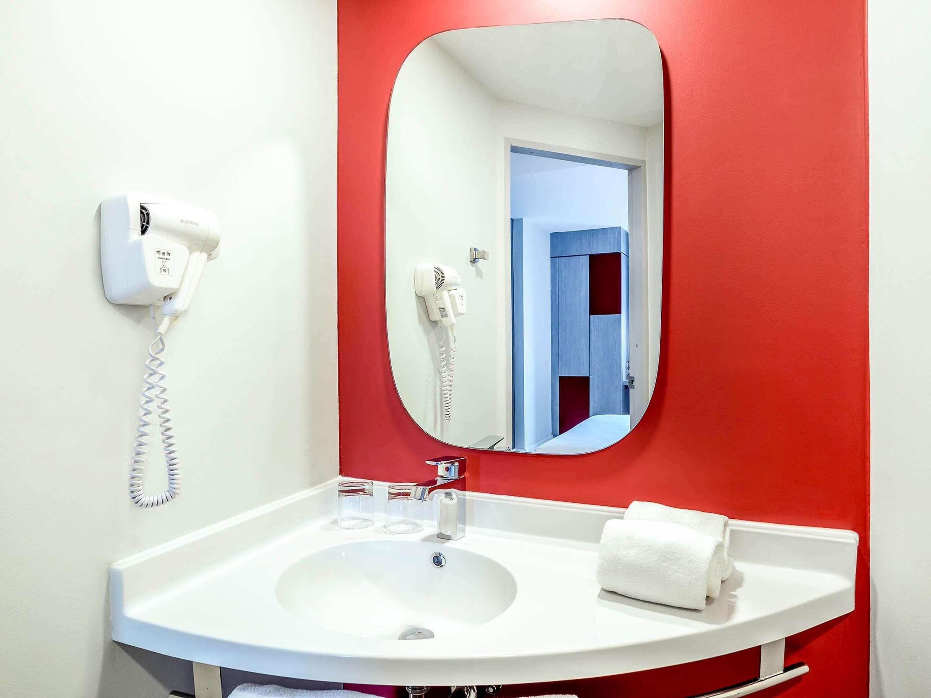 Un baño con un lavabo blanco, una pared roja, un espejo, un secador de pelo y un teléfono.