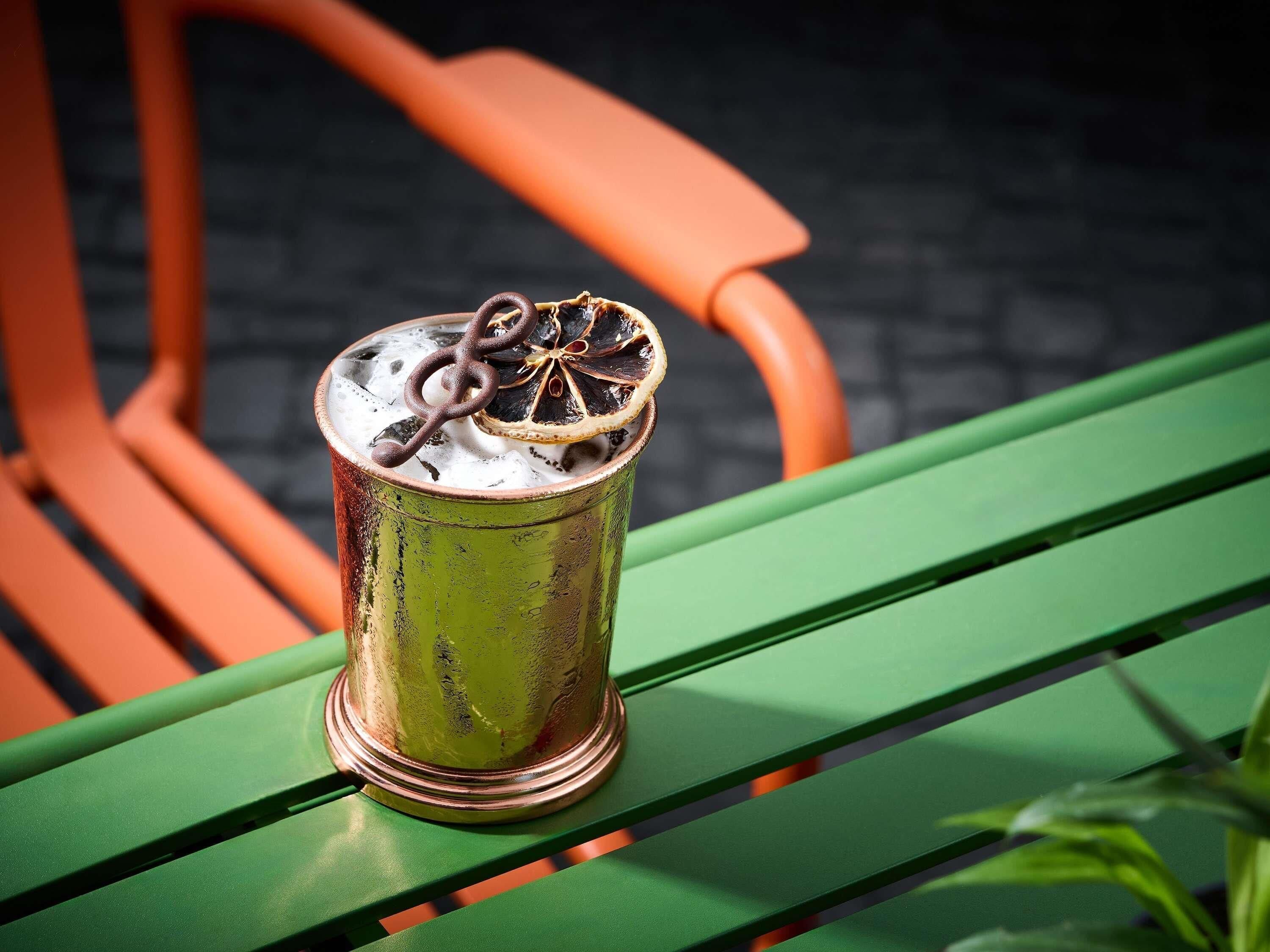 A metallic cup with a decorative item on a green bench.