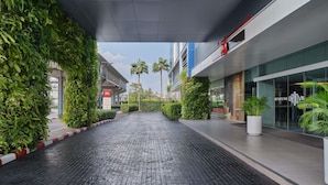 A modern hotel entrance with a brick pathway, greenery, and a clear sky. - ibis Bangkok IMPACT (Pak Kret)