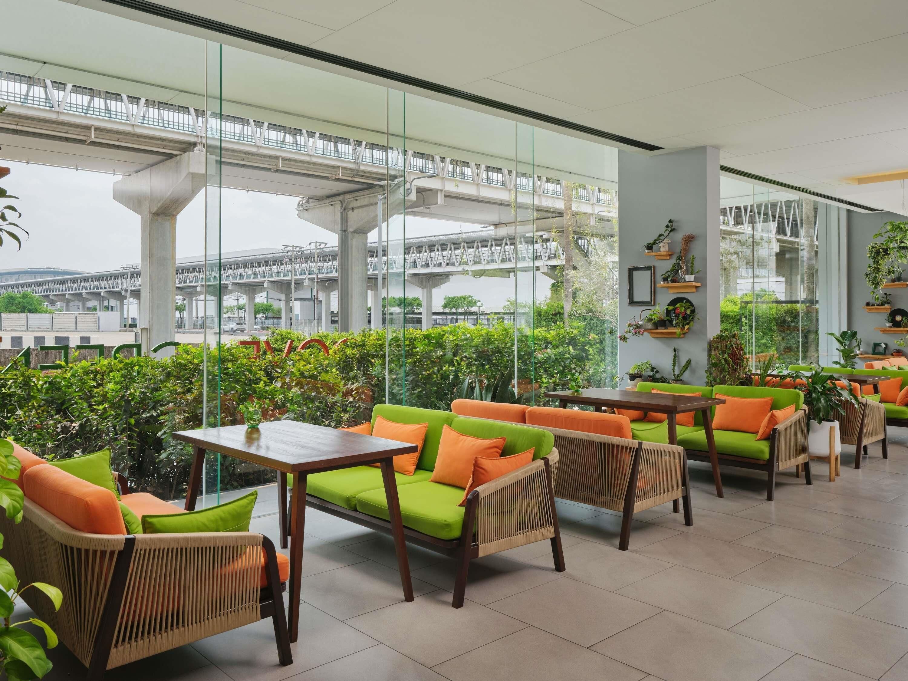 A modern indoor seating area with glass walls, green and orange furniture, and a view of a bridge.