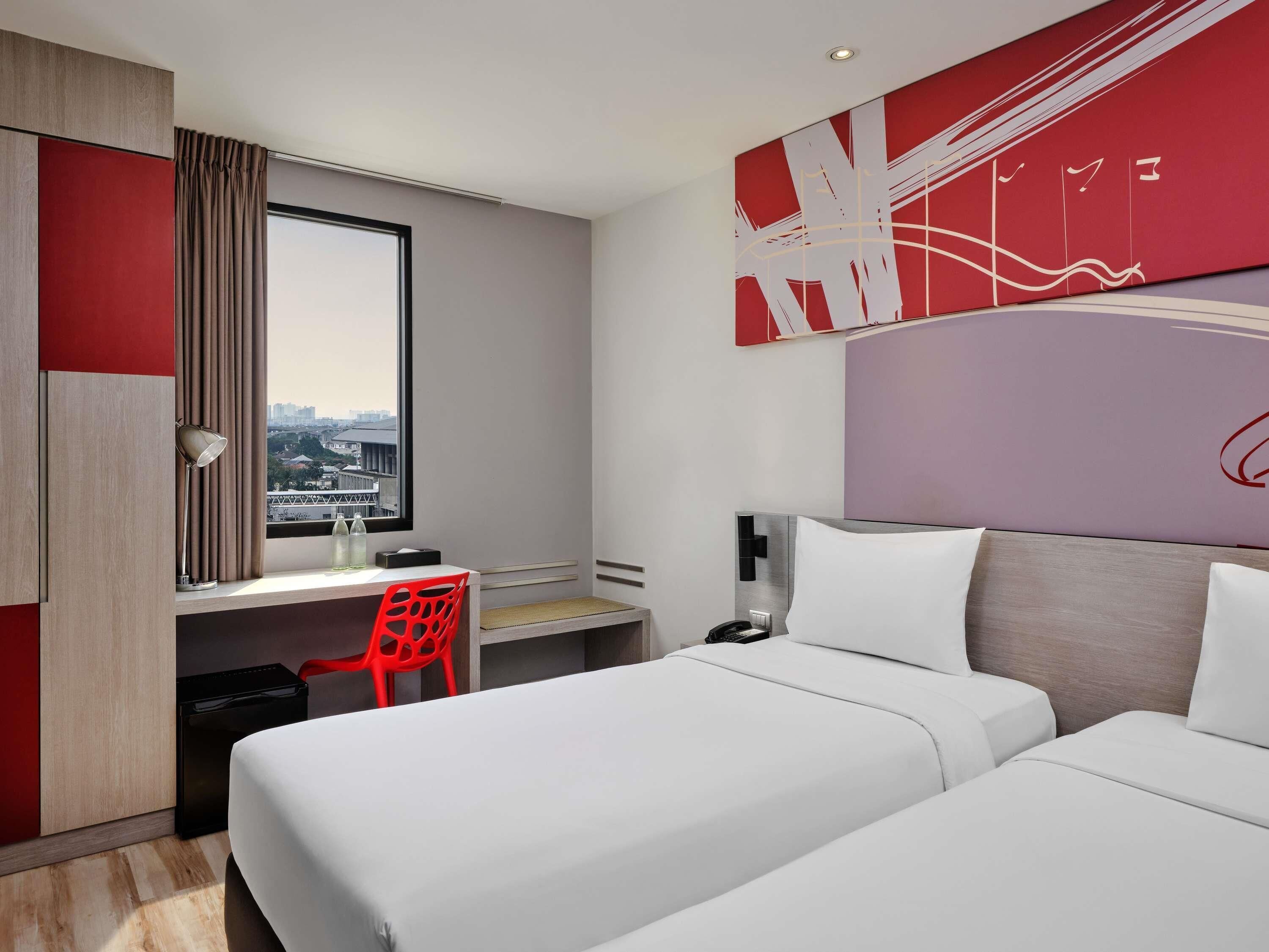 A hotel room with a bed, a desk, a chair, and a window with a city view.