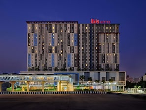 A multi-story hotel with a modern design, featuring a prominent 'ibis HOTEL' sign at the top.