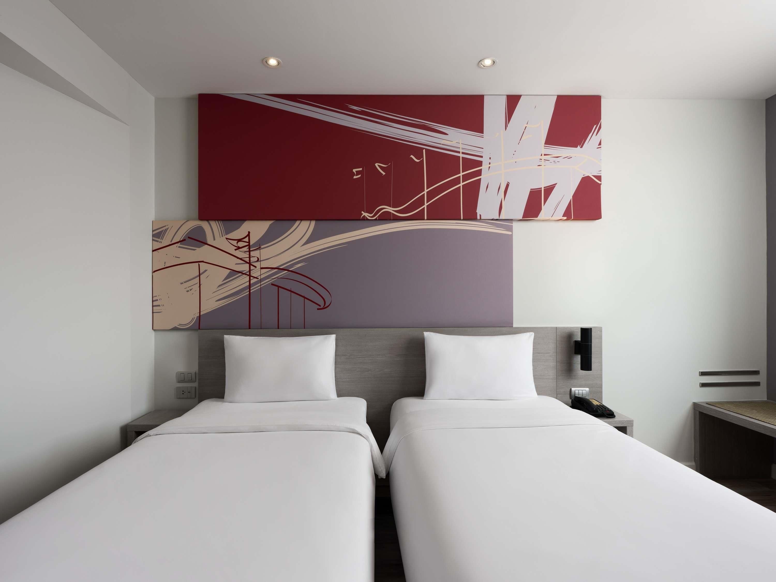A hotel room with two beds, a large abstract painting on the wall, and a nightstand with a phone.