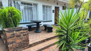 Un patio con pared de ladrillo, una mesa redonda y bancos.
