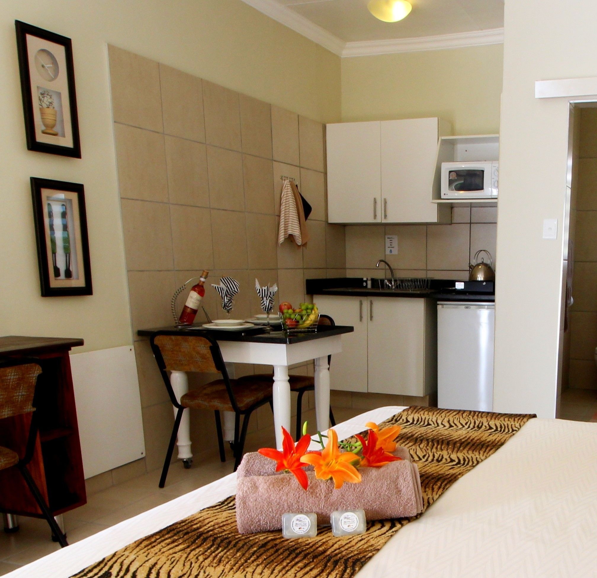 A hotel room with a bed, a dining table with chairs, a kitchen area with cabinets and appliances, and a bathroom visible through an open door.