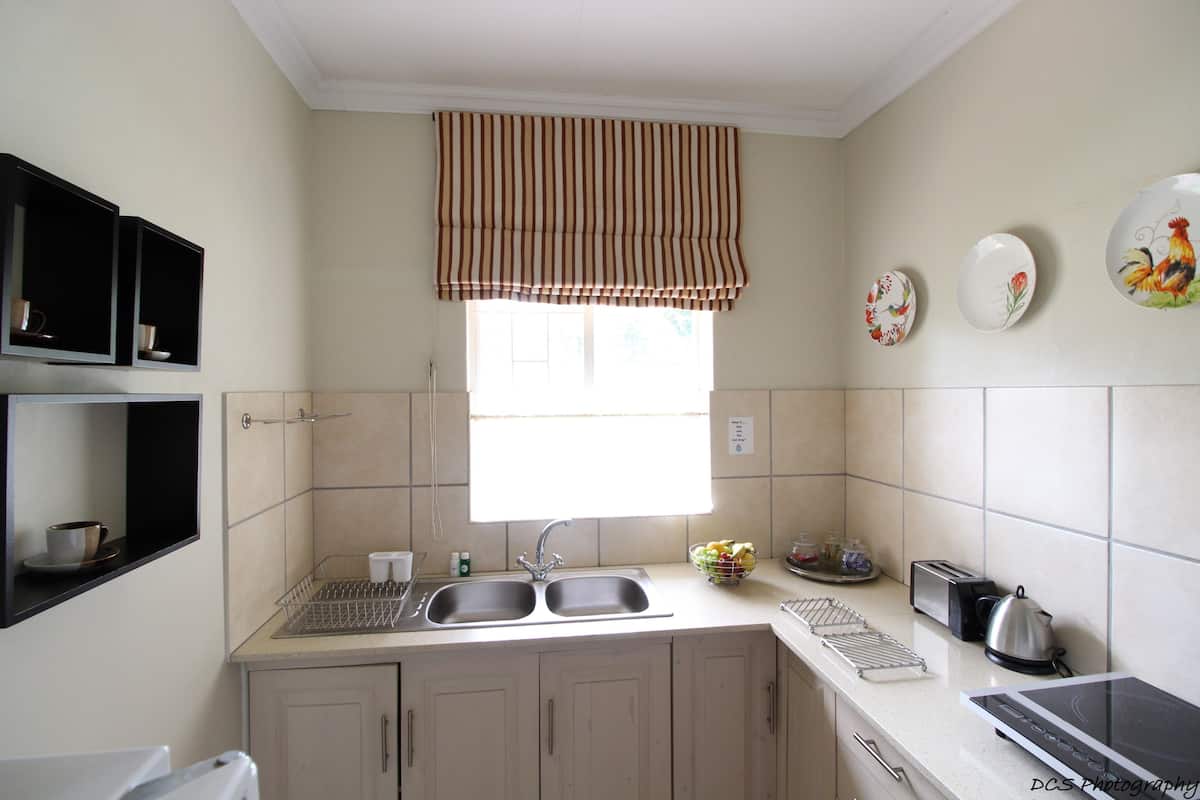 A kitchen with a double sink, a window with a striped valance, and a toaster.