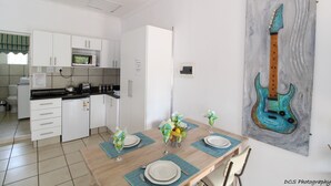 Una cocina moderna con armarios blancos, un microondas y un comedor con una mesa preparada para cuatro.