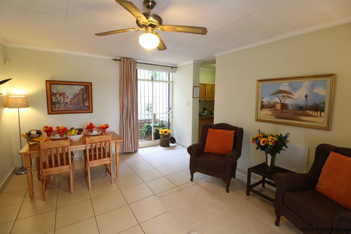 A living room with a dining table set for four, a ceiling fan, and two armchairs.