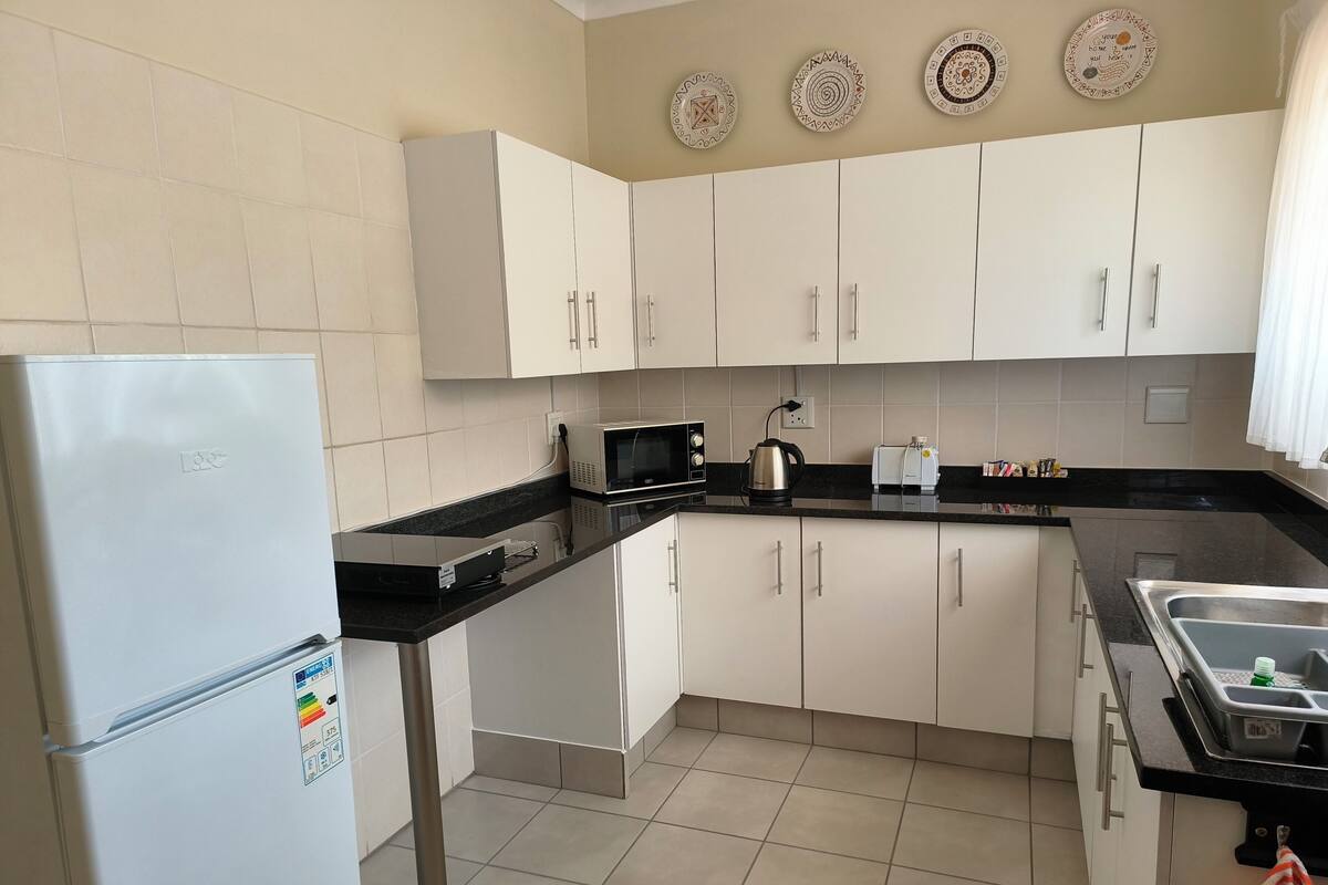 A modern kitchen with white cabinets, a refrigerator, a microwave, a kettle, and a toaster.