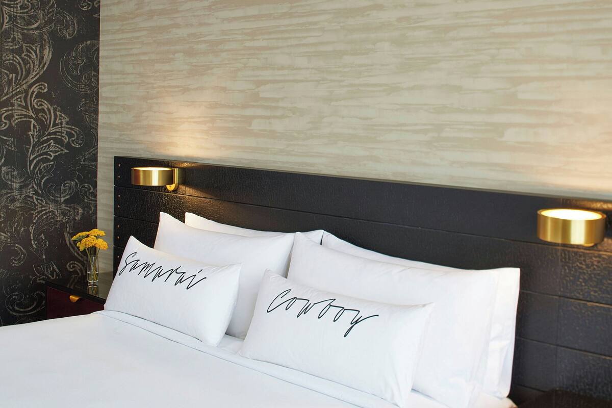 A neatly made bed with white linens and two pillows with cursive text. There is a wall-mounted light fixture above the bed.