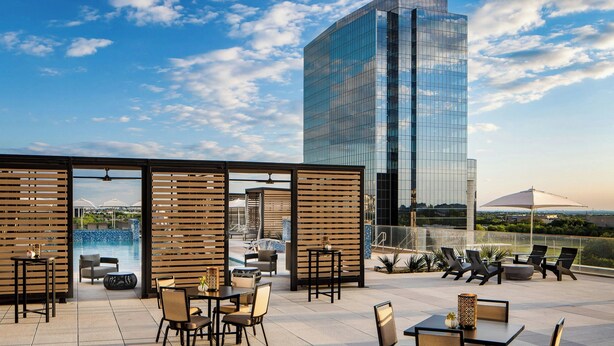 A rooftop terrace with outdoor seating, a pool, and a view of a modern glass building. - Renaissance Dallas at Plano Legacy West Hotel (Plano)