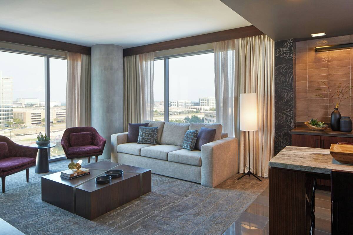 A modern living room with a sofa, armchairs, a coffee table, and a view of the city through large windows.