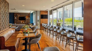 A modern restaurant with wooden tables and chairs, a bar area, and large windows offering a city view. - Renaissance Dallas at Plano Legacy West Hotel (Plano)