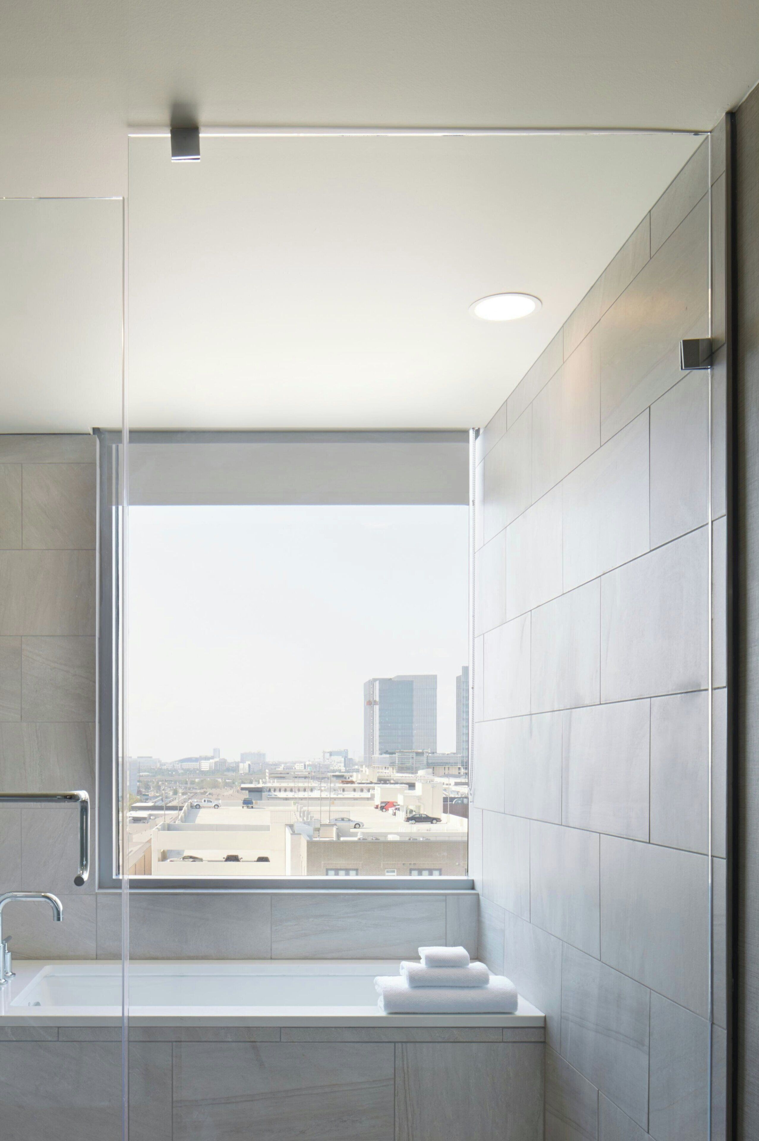 A modern bathroom with a large window, a bathtub, and a shower area.