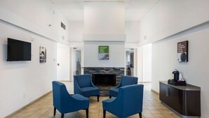 A lobby with a fireplace, blue armchairs, a flat-screen TV, and a coffee station. - Studio 6 Irving, TX - Irving DFW Airport East (Irving)