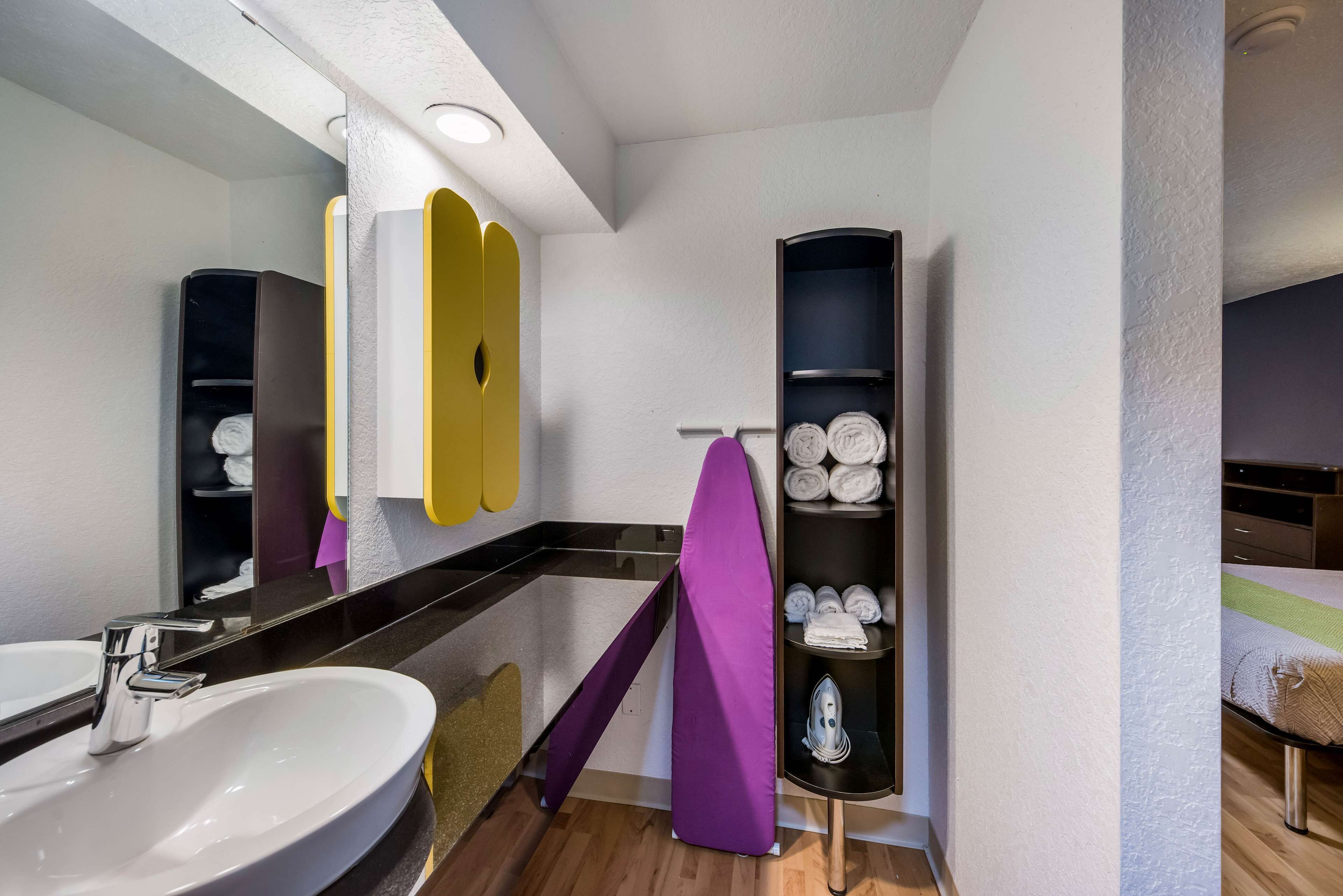 A modern bathroom with a large sink, a mirror, a towel rack, and a shelf with neatly folded towels.