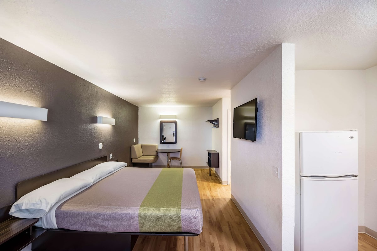 A hotel room with a bed, a small table, a chair, a television, and a refrigerator.