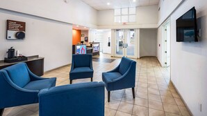 A lobby with blue chairs, a reception desk, a TV, and a sign about morning charge. - Studio 6 Irving, TX - Irving DFW Airport East (Irving)