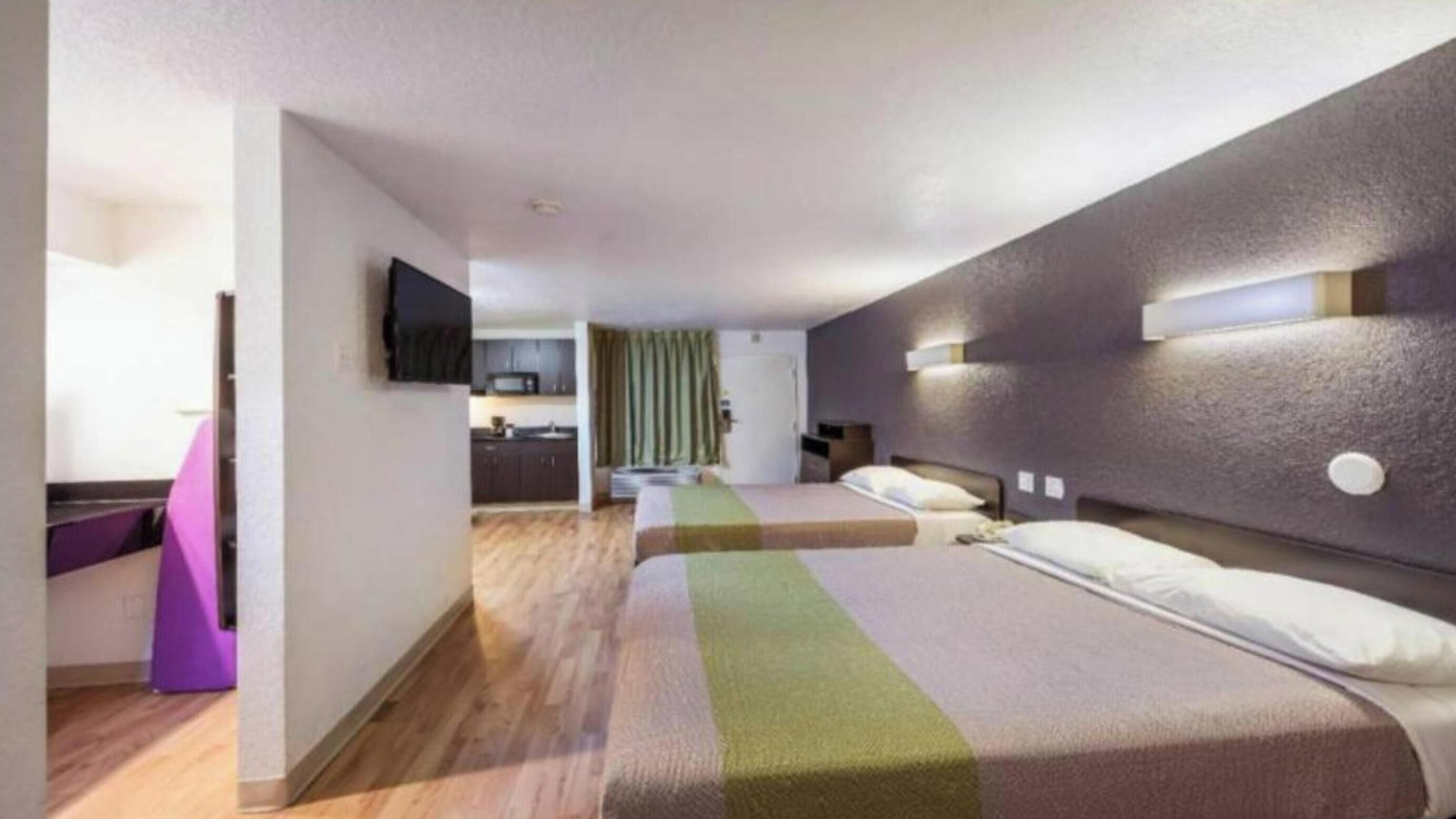 A hotel room with a bed, a desk, a chair, a television, and a kitchenette.
