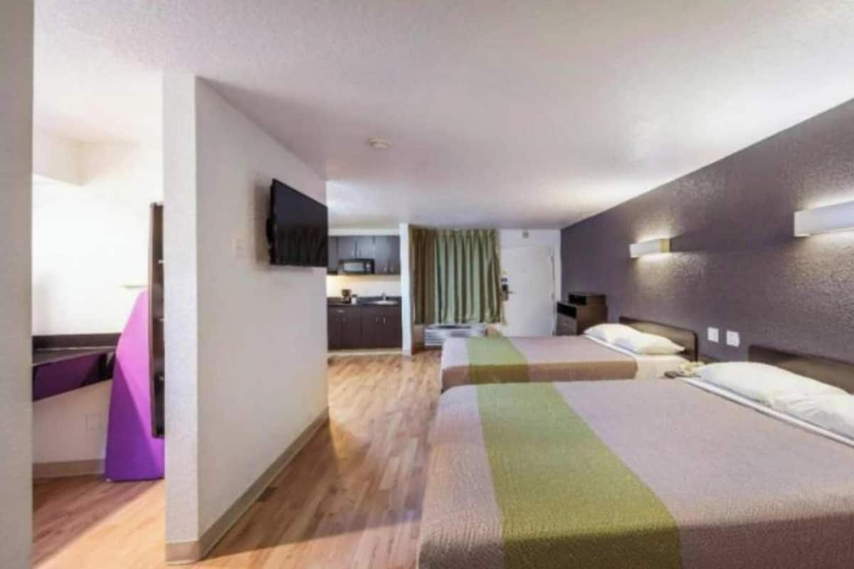 A hotel room with a bed, a desk, a chair, a television, and a kitchenette.