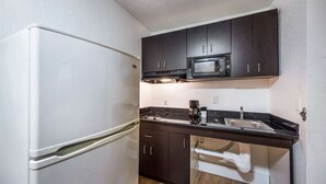A compact kitchen with a white refrigerator, dark cabinets, a microwave, a sink, and a white countertop. - Studio 6 Irving, TX - Irving DFW Airport East (Irving)