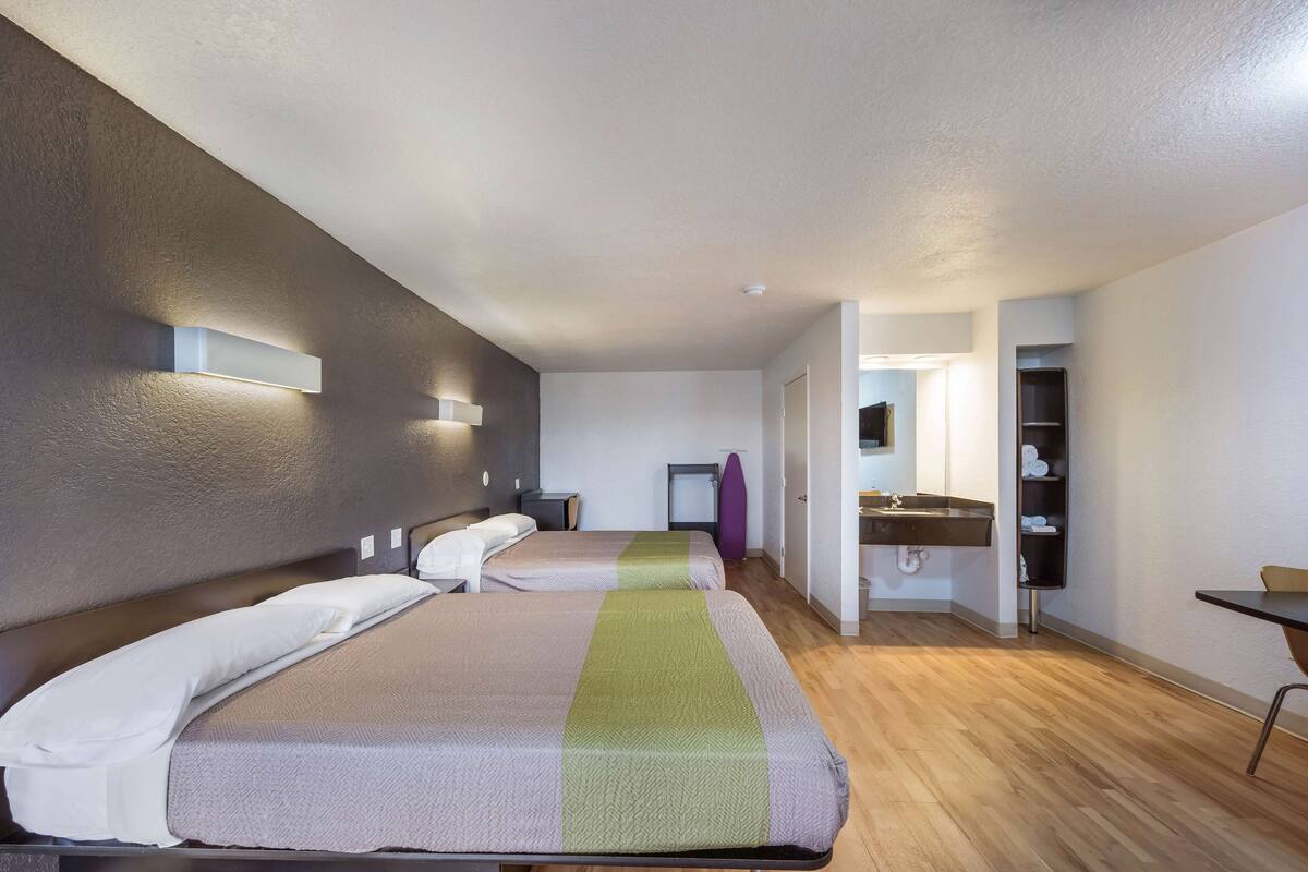A hotel room with two beds, a bathroom with a sink, and a small table.