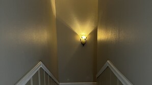 Un corridoio stretto con una parete strutturata, un lampadario e una scala rivestita di moquette.
