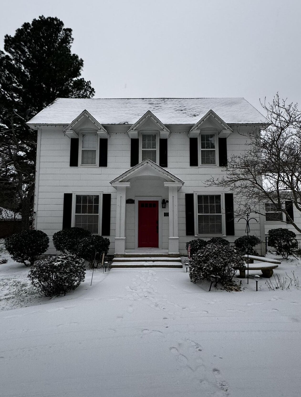 A two-story house with a red door and a snow-covered front yard.