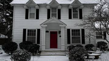 A two-story house with a red door and a snow-covered front yard.