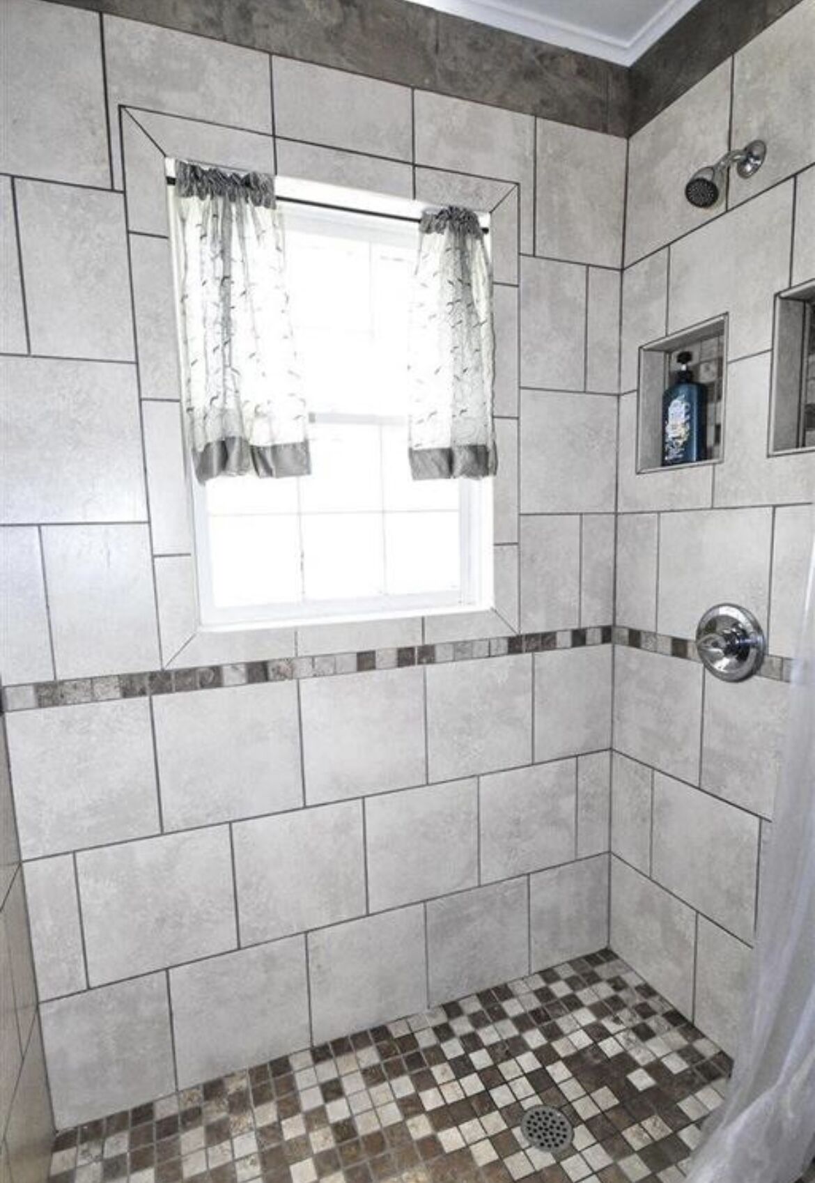 Un baño con ventana, paredes de azulejos, zona de ducha y suelo de cuadros.