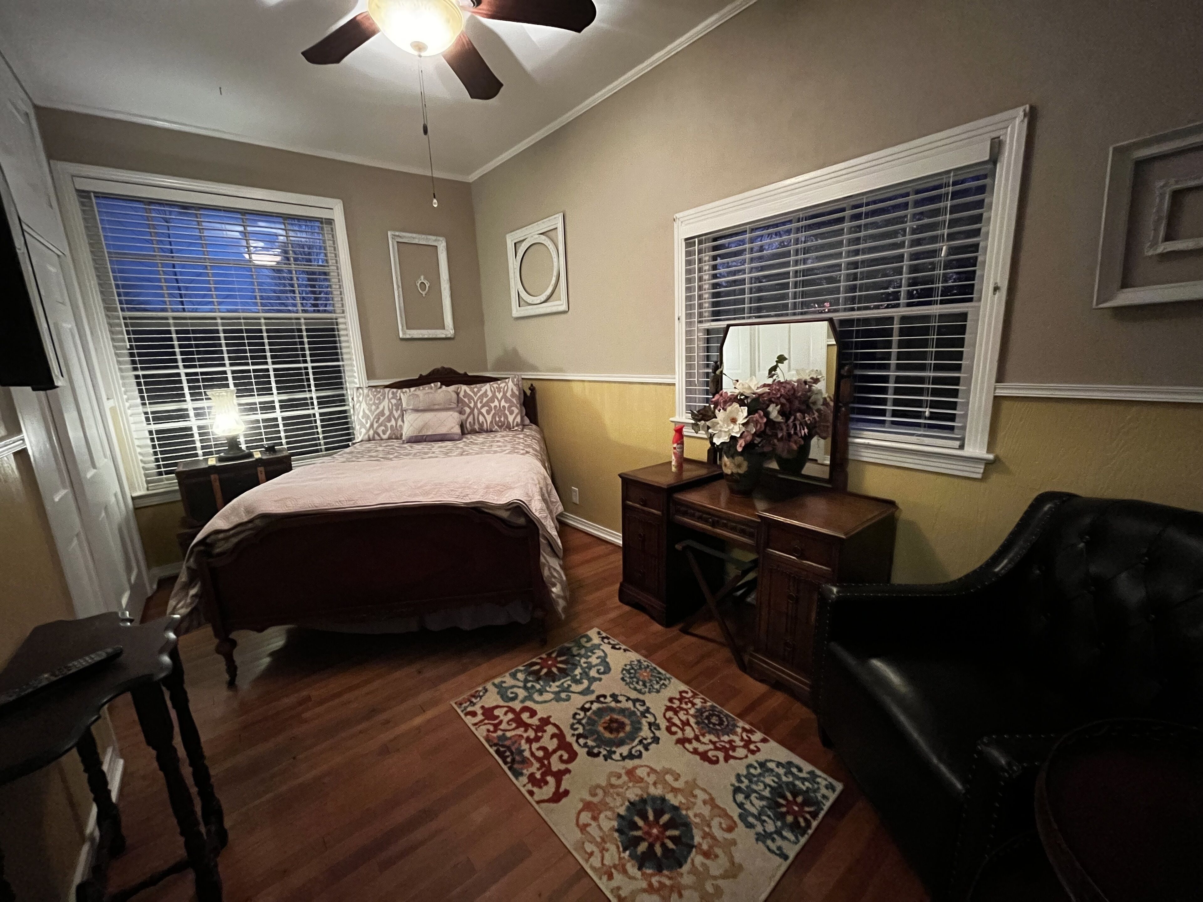 A bedroom with a bed, dresser, chair, and a ceiling fan.