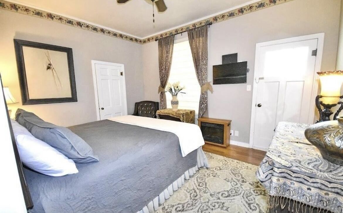 A bedroom with a large bed, a nightstand, a chair, a desk, and a lamp.