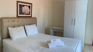 Una cama bien hecha con sábanas y almohadas blancas, un cuadro en la pared y un armario blanco.