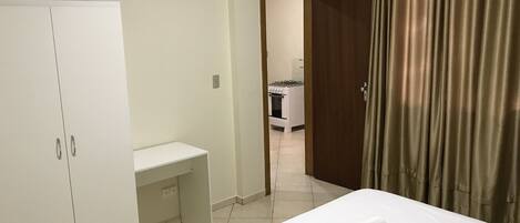 Habitación de hotel con cama, escritorio, armario y baño visible a través de una puerta abierta.
