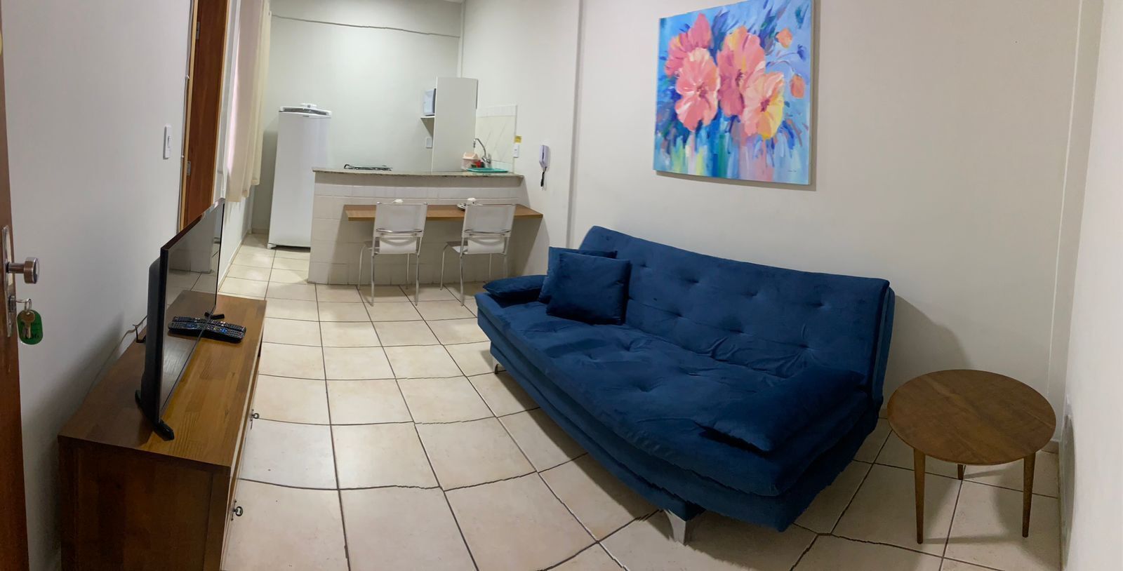 A living room with a blue sofa, a small round table, and a kitchen area in the background.