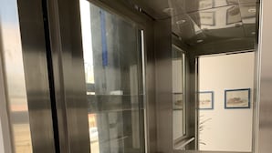 Interior moderno de ascensor con paredes metálicas, paneles de vidrio y suelo de madera.