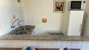 Una cocina con encimeras de granito, un fregadero, un microondas y un refrigerador. Hay dos sillas blancas con patas de madera y una mesa con individuales azules.