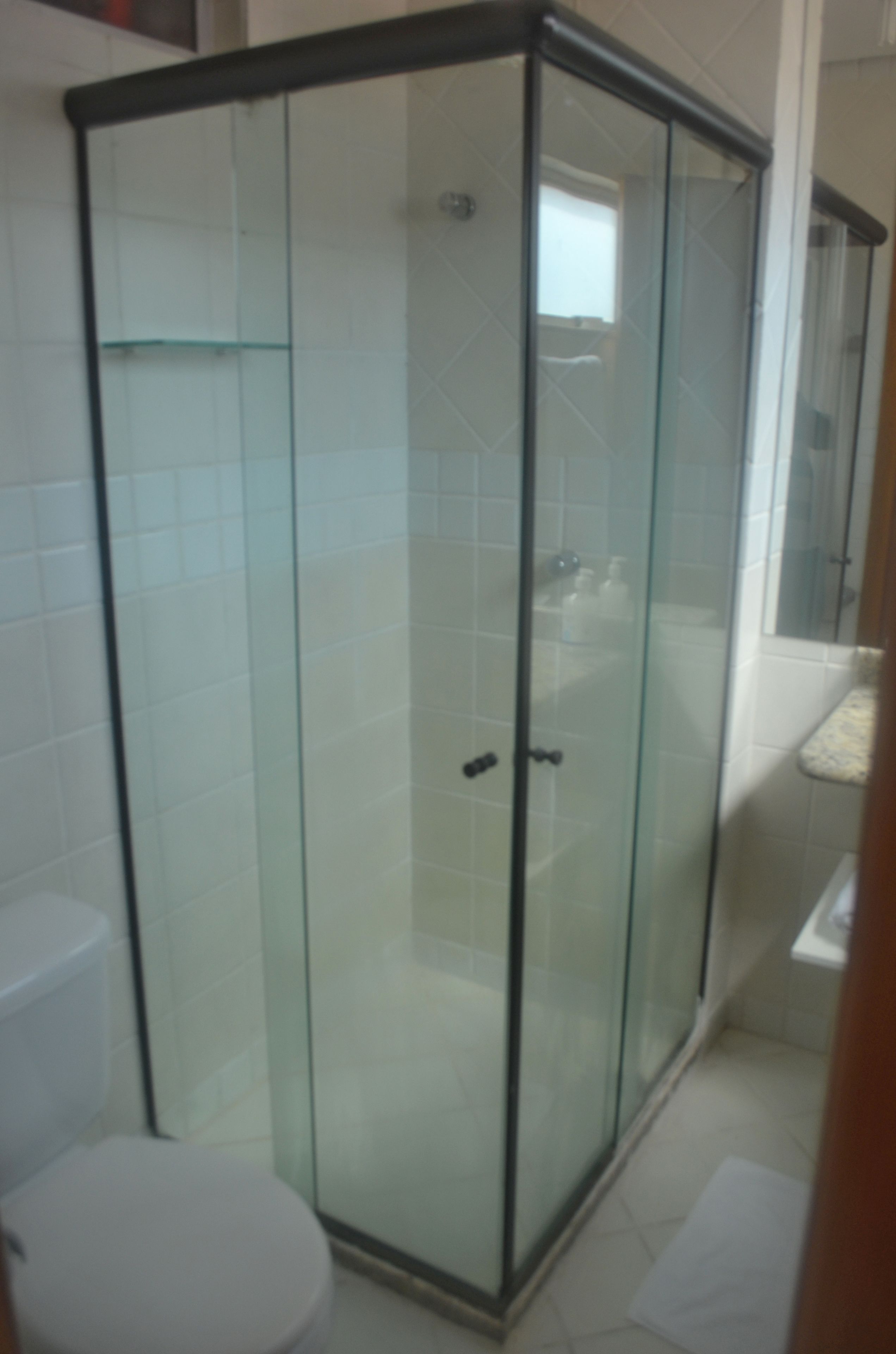 Une salle de bain avec une douche à parois de verre, des toilettes blanches et un carrelage au sol.